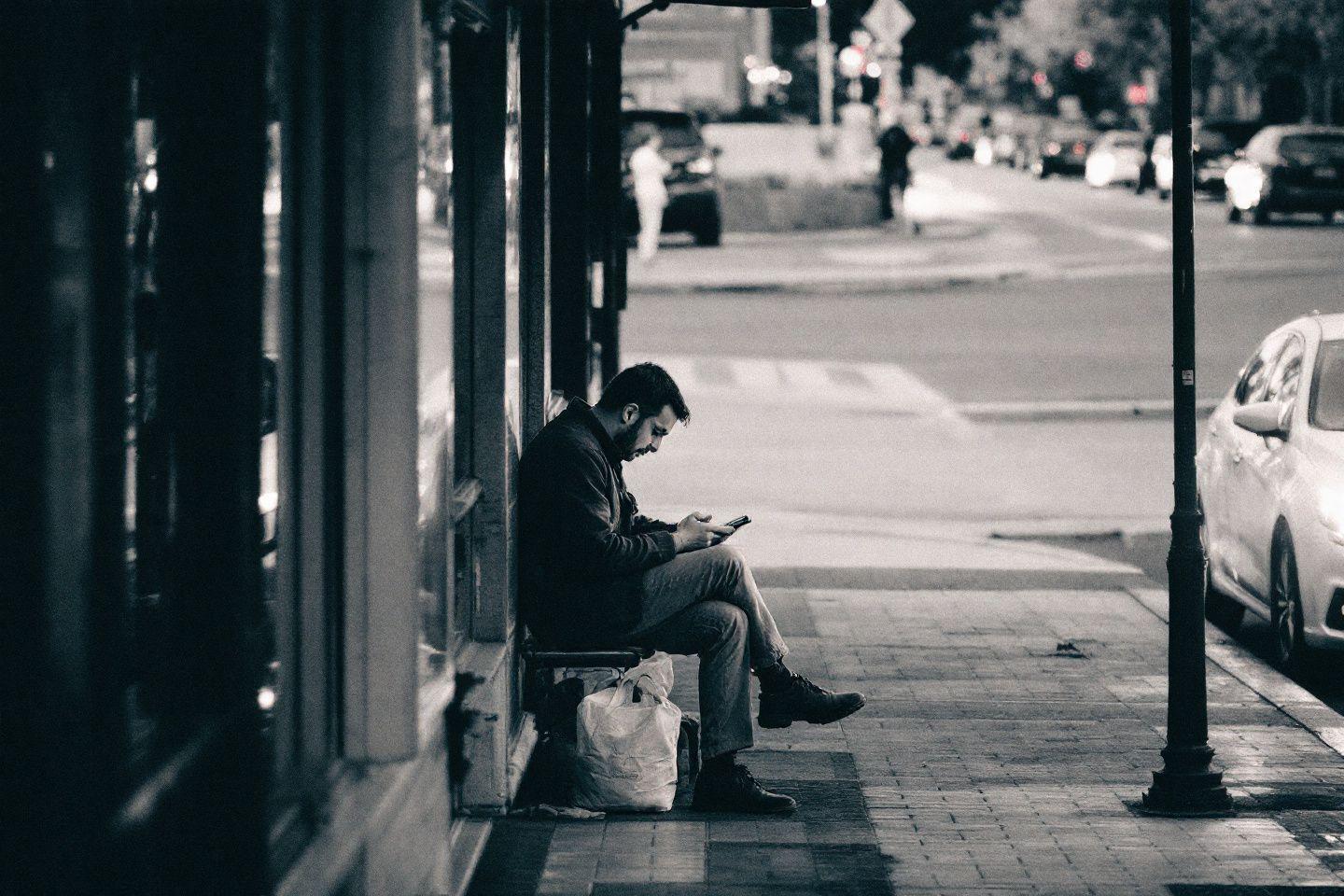 Homme assis sur un banc public, entouré de bâtiments et de voitures